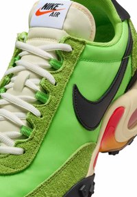 Baskets Nike Air vertes avec swoosh noir, lacets blancs, détails en daim texturé et une semelle crème avec un coussin d'air rouge.