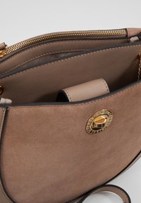 Borsa a mano in pelle marrone con texture scamosciata, accessori in oro, chiusura con zip e tasca interna. Presenta una forma arrotondata con un accento a catena.