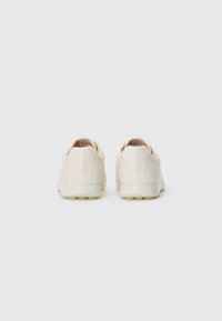 Une paire de baskets blanches à lacets montrée de dos sur un fond gris clair uni.