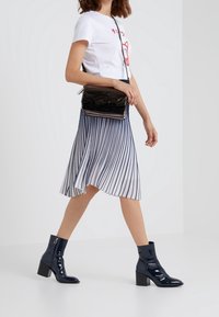 T-shirt bianco con grafica rossa, gonna midi plissettata blu scuro e stivaletti blu scuro lucidi con tacco a blocco. Borsa a tracolla nera con dettagli.