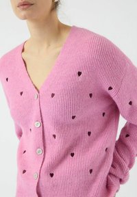 Rosa gerippter Cardigan mit V-Ausschnitt, vorderen Knöpfen und kleinen dunklen Herzmustern. Hergestellt aus weichem Textilmaterial.