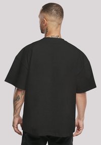 Černé oversized tričko vyrobené z bavlny, s kulatým výstřihem, spadlými rameny a krátkými rukávy. Hladká textura bez vzorů.