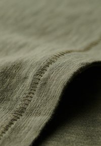 Primer plano de tela verde oliva que muestra costuras detalladas a lo largo de una costura con un material de punto suave y texturizado.