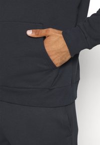 Sweatshirt marine foncé avec une poche frontale, des poignets et un ourlet côtelés. La texture du tissu semble lisse et décontractée dans son design.