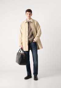 Μπεζ εξωτερικό παλτό με κούμπωμα, καφέ φούτερ, σκούρα μπλε τζιν και μαύρη δερμάτινη τσάντα. Μαύρα παπούτσια με καουτσούκ ολοκληρώνουν την εμφάνιση.