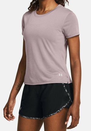 Mujer vestida con una camiseta deportiva de manga corta color lavanda y pantalones cortos negros para correr con ribete estampado, de pie contra un fondo liso.