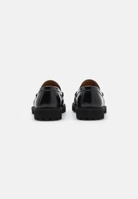Chaussures en cuir verni noir avec une finition lisse, bout arrondi et semelle en caoutchouc noir robuste dotée de crampons texturés.