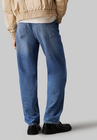 Jeans din denim de un albastru deschis, cu o croială relaxată, având buzunare la spate și o ușoară decolorare. Asortați cu pantofi negri și o jachetă bomber de culoare bej.
