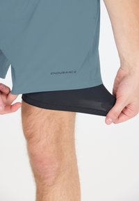 Helle blaue Sportshorts mit schwarzem Innenfutter, die eine glatte Textur aufweisen, das Logo "ENDURANCE" auf der linken Seite tragen und in einem lässigen Schnitt gehalten sind.