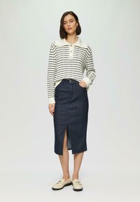 Gestreifter Pullover in Weiß und Marineblau mit Kragen, kombiniert mit einem dunklen Jeansrock mit Schlitz vorne. Die Schuhe sind beigen Slipper.