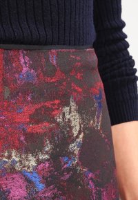 Gros plan sur une personne portant un pull côtelé bleu marine et une jupe taille haute avec un motif abstrait rouge, violet et bleu.