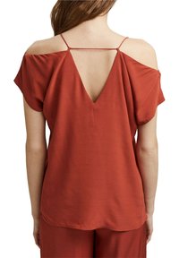 Blusa de color óxido con escote en V en la espalda, mangas cortas y tirantes finos. Textura suave y corte relajado, con un dobladillo redondeado.