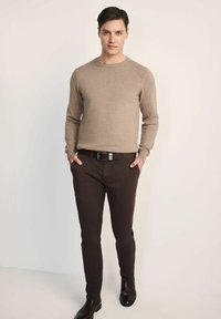 Beżowy sweter robiony na drutach z okrągłym dekoltem, w połączeniu z ciemnobrązowymi spodniami slim-fit i czarnymi skórzanymi butami, tworząc casualowy zestaw.