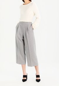 Valkoinen neulepaita, jossa on tekstuuri-kuvio ja pyöreä pääntie, yhdistettynä korkeavyötäröisiin harmaisiin leveälahkeisiin housuihin ja mustiin hihnallisiin korkokenkiin.