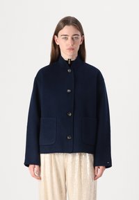 Marineblaues Wolljackett mit hohem Kragen, Knopfschluss und zwei vorderen Taschen. Es hat eine lockere Passform und eine glatte Textur.