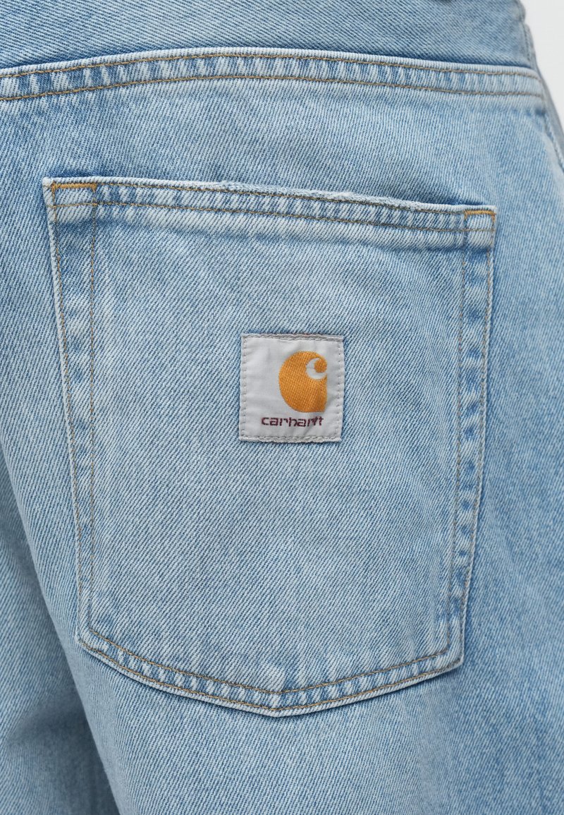 Hellblaue Jeansshorts mit einer Gesäßtasche, die ein weißes Etikett, ein oranges Logo und kontrastierende Nähte aufweist. Glatte Textur und klassisches Design.