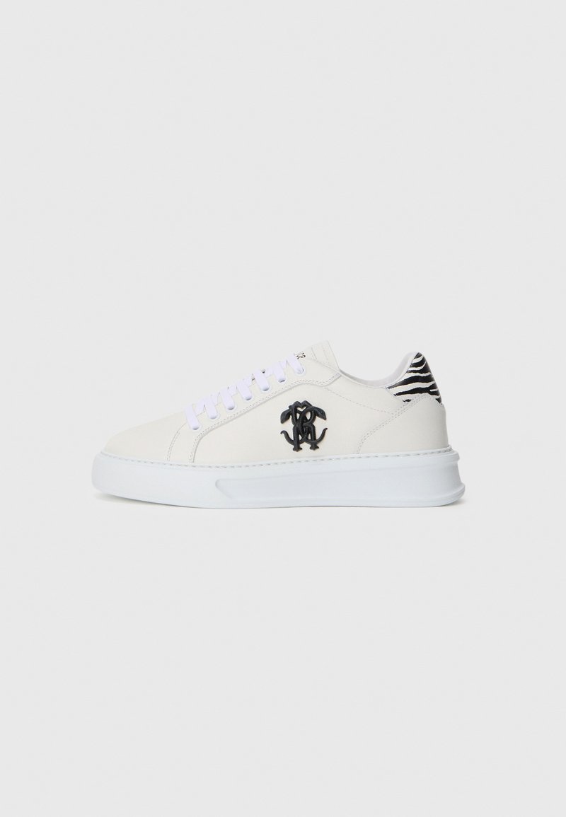 Adidași din piele albă cu un logo negru pe lateral, șireturi mov și un accent de călcâi în dungi alb-negru. Talpă groasă albă.