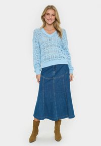 Jasnoniebieski, dziergany sweter z koronkowym wzorem i dekoltem w kształcie V; zestawiony z dżinsową spódnicą. Modelka nosi brązowe zamszowe botki za kostkę.