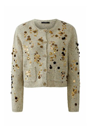 Lichtgrijze cropped cardigan met gouden en zwarte sequins, gestructureerde stof, ronde halslijn en twee voorkwasten. Sluiting met vier knopen.