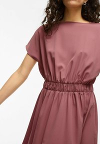 Mauve, kratka obleka s kratkimi rokavi in sproščenim krojem, ki ima elastičen pas in tokovito krilo, izdelana iz gladkega materiala.