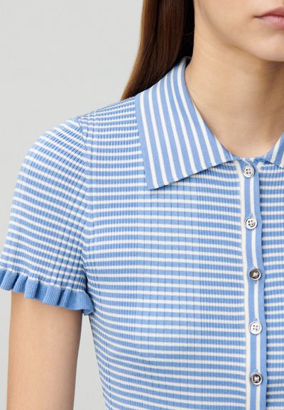 Camisa polo a rayas azul y blanca con textura acanalada, mangas cortas con volantes y cierre de botones con botones decorativos.