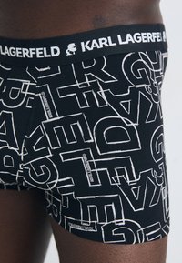 Schwarze Boxershorts mit auffälligen, kontrastierenden weißen Buchstaben und einem Markenbund mit "KARL LAGERFELD". Hergestellt aus weichem, dehnbarem Stoff.