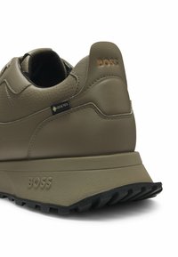 Olivgrön sneaker i texturerat läder med släta detaljer. Har en gummisula och en Gore-Tex-tagg som visar "BOSS"-profil.