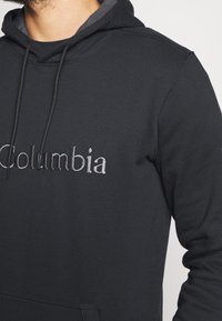 Felpa nera con cappuccio, tasca frontale a marsupio, coulisse per il cappuccio e scritta "Columbia" ricamata a contrasto sul petto.
