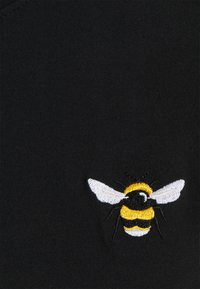 Camiseta de algodón negra con un detallado bordado de una abeja en amarillo, negro y blanco, situada en la parte delantera cerca del dobladillo.