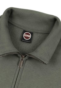 Grön zip-jacka med ribbad krage, mjukt inre och metallisk dragkedja. Har en Colmar Originals-etikett på nacken.