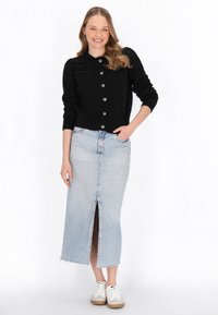 Svart stickad kofta med hjärtformade knappar, ljusblå denim midi kjol med framreva och vita sneakers med beige detaljer.