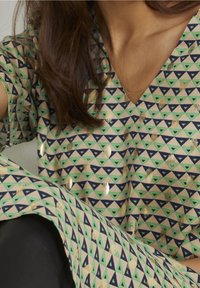 Mönstrad tunika med V-ringning, beige bakgrund med gröna och marinblå trianglar, samt gyllene inslag genom tyget.