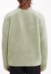 Groene fleece jas met een gestructureerd, pluizig oppervlak, voorzien van een kraag en verlaagde schouders. De achterkant is effen zonder patronen.