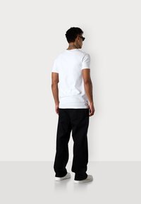 Weißes T-Shirt mit kurzen Ärmeln und Rundhalsausschnitt, kombiniert mit locker sitzenden schwarzen Hosen und weißen Sneakers. Enthält ein kleines Logo am Saum.