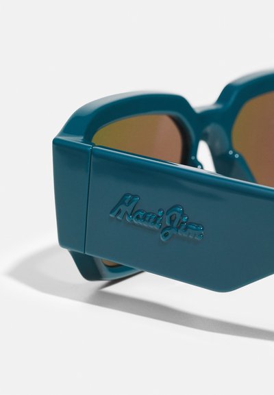 Türkiz napszemüveg, fényes felülettel, nagyméretű négyzet alakban, borostyán színű lencsékkel és dombornyomott "Maui Jim" logóval a szárán.