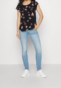 Haut noir à manches courtes avec un motif floral rose, associé à un jean skinny bleu clair et des baskets blanches. Coupe droite à l'ourlet.