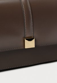 Rjava usnjena torba z gladko teksturo, nežnimi šivi in zlatim štirikotnim zaponkom za zapiranje.