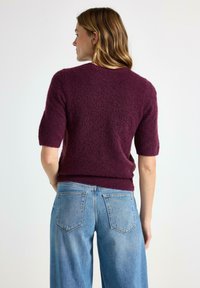 Burgunderfarvet strikket sweater med korte ærmer og tekstureret overflade, parret med højtaljede lyseblå denim jeans.