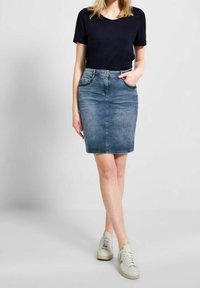 Ljusblå denimkjol med figursydd design, ovanför knäna, med framfickor och knappstängning. Matchad med en svart t-shirt och sneakers.