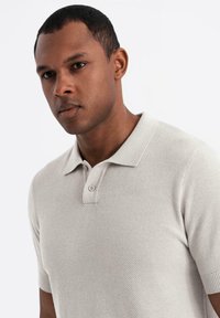 Camisa polo de color gris claro con tejido texturizado, mangas cortas, un cuello clásico y dos botones en el cuello.