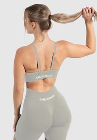 Conjunto deportivo gris que incluye un sujetador elegante y pantalones cortos de cintura alta con un corte en la espalda y el logo en blanco "SMILODOX" en la banda. Textura suave.