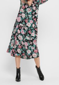 Kukkamekko V-purkilla, jossa on isot vaaleanpunaiset ja teal-väriset kukat mustalla taustalla. Slim fit -malli, lyhyet hihat ja polvipituinen helma.