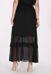 Schwarzes Chiffonkleid mit Punkten, gerafftem Saum und geschichtetem Design. Sichtbare Riemchen-High-Heelsandalen.