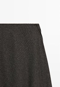 Mørkegrå og sort houndstooth-mønstrede stof med en synlig søm på en hvid baggrund.