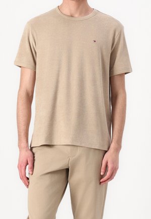 Beżowa bawełniana koszulka z krótkim rękawem, okrągłym dekoltem i małym logo na piersi. Miękki materiał i luźny krój. Połączona z beżowymi spodniami.