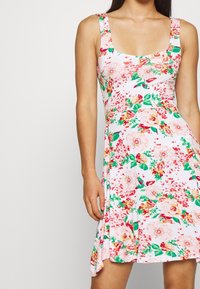 Robe florale à base rose, décolleté carré et bretelles larges. Fleurs vives en rose, rouge et vert sur l'ensemble du tissu.