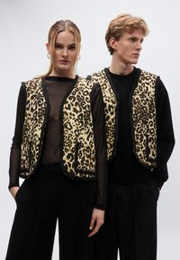 Puha anyagból készült párducmintás mellények, fekete szegéllyel, áttetsző felsők fölött viselve. Az egyik mellény zsebdísszel rendelkezik. Fekete nadrágok egészítik ki a ruhákat.