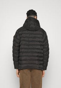 Giacca puffer nera con cappuccio, caratterizzata da un design trapuntato e polsini elastici. Il tessuto ha una superficie liscia e lucida.