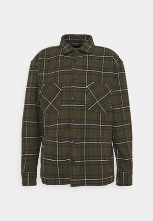 Camisa de franela verde oscura con un patrón de cuadros en blanco y negro, que cuenta con un cierre frontal con botones, dos bolsillos en el pecho y un collar.