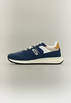Marineblå joggesko med hvite og sennepsfargede detaljer, hvite snørebånd, og "JACK & JONES"-logo på siden, mot en enkel nøytral bakgrunn.